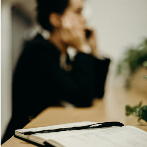 Women on table talking to someone on the phone with a notebook in foreground.